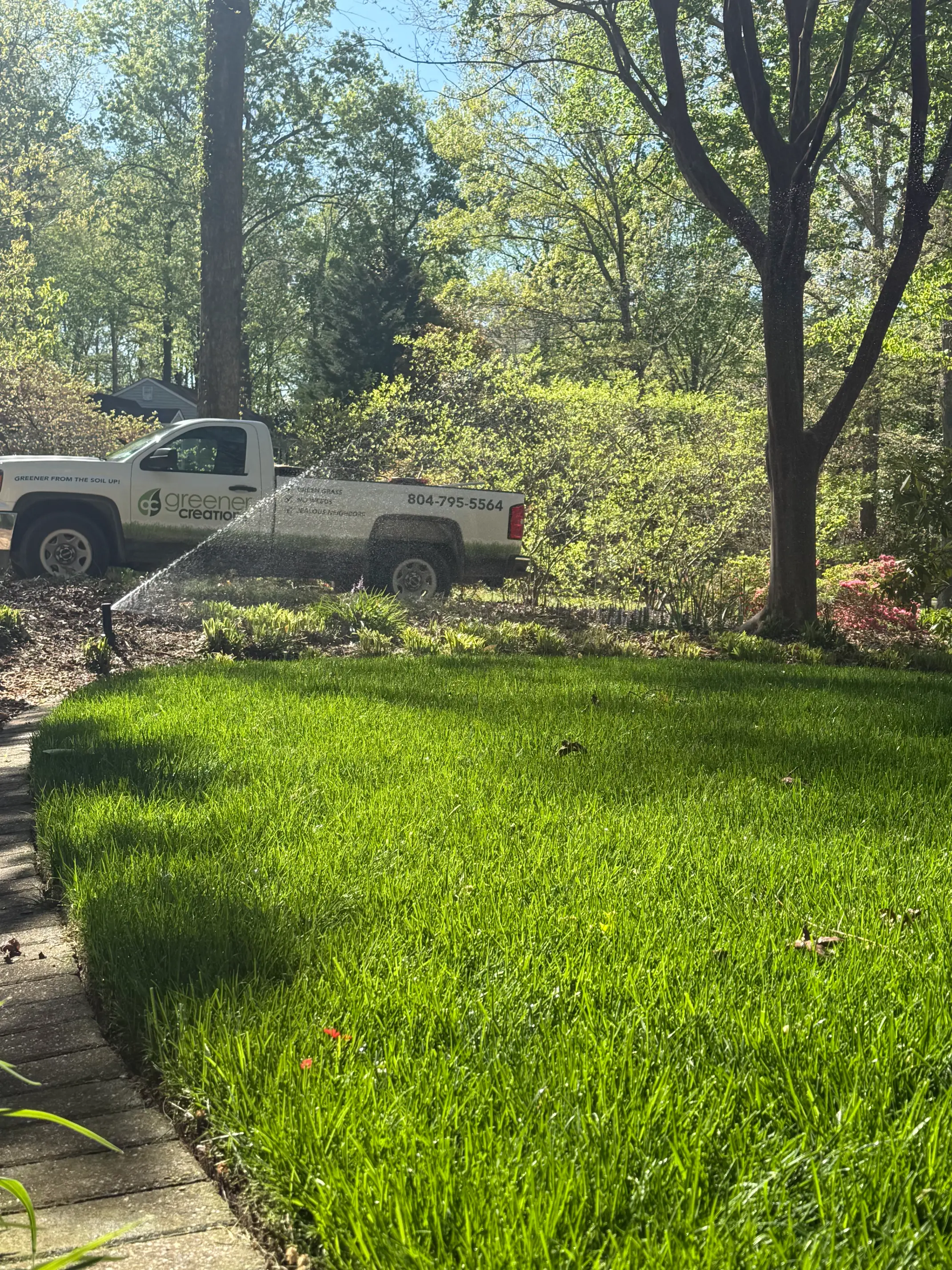 Sprinkler head spraying over treated lawn with truck in background - Professional lawn care services in Richmond, VA